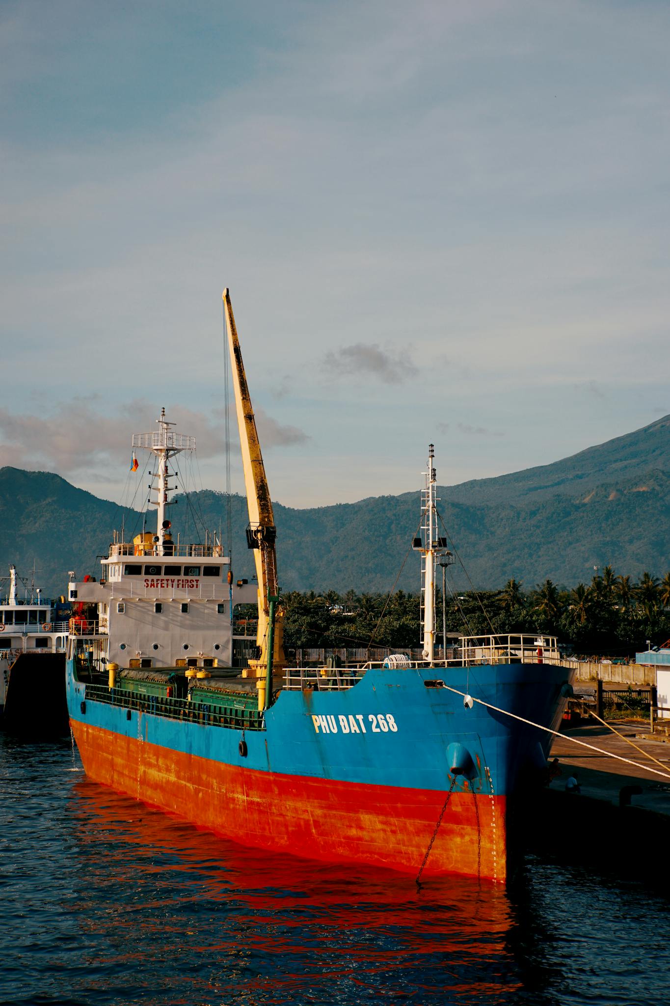 A vibrant cargo ship docked at a port with a mountain backdrop, ideal for travel and transportation themes.
